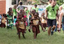 Otroci s prostovoljci v Gambiji, ki tečejo na travniku. Imajo športni dan